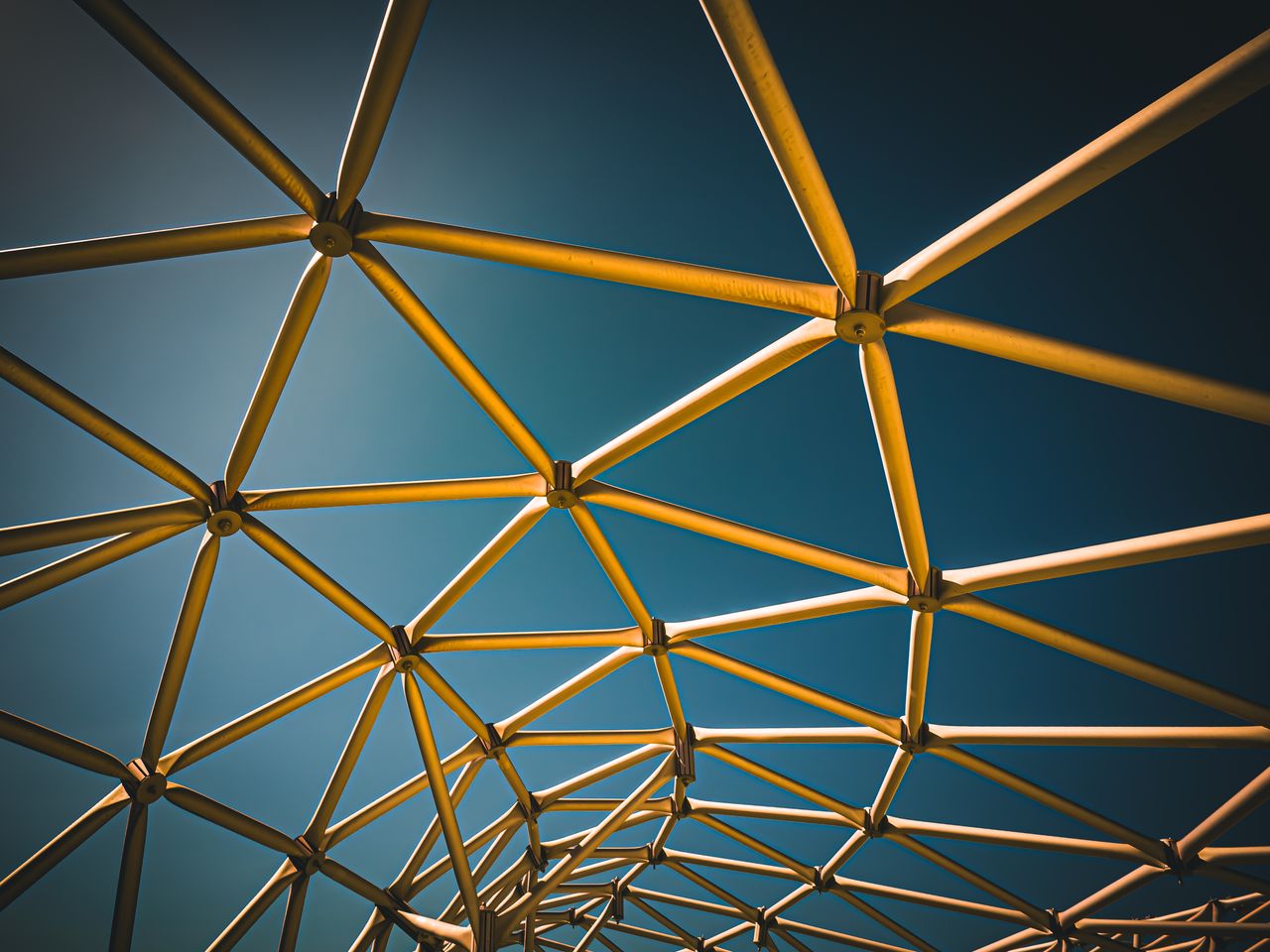 Dynamic geometric metal structure with triangular patterns against a blue sky, showcasing modern architectural design.