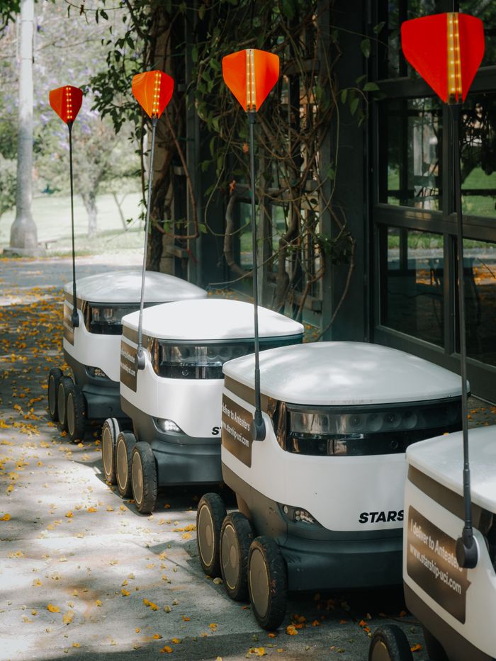 Row of futuristic autonomous delivery robots parked outdoors, showcasing modern technology.